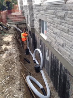 Under 44 worker installing waterproofing pipes at a foundation wall